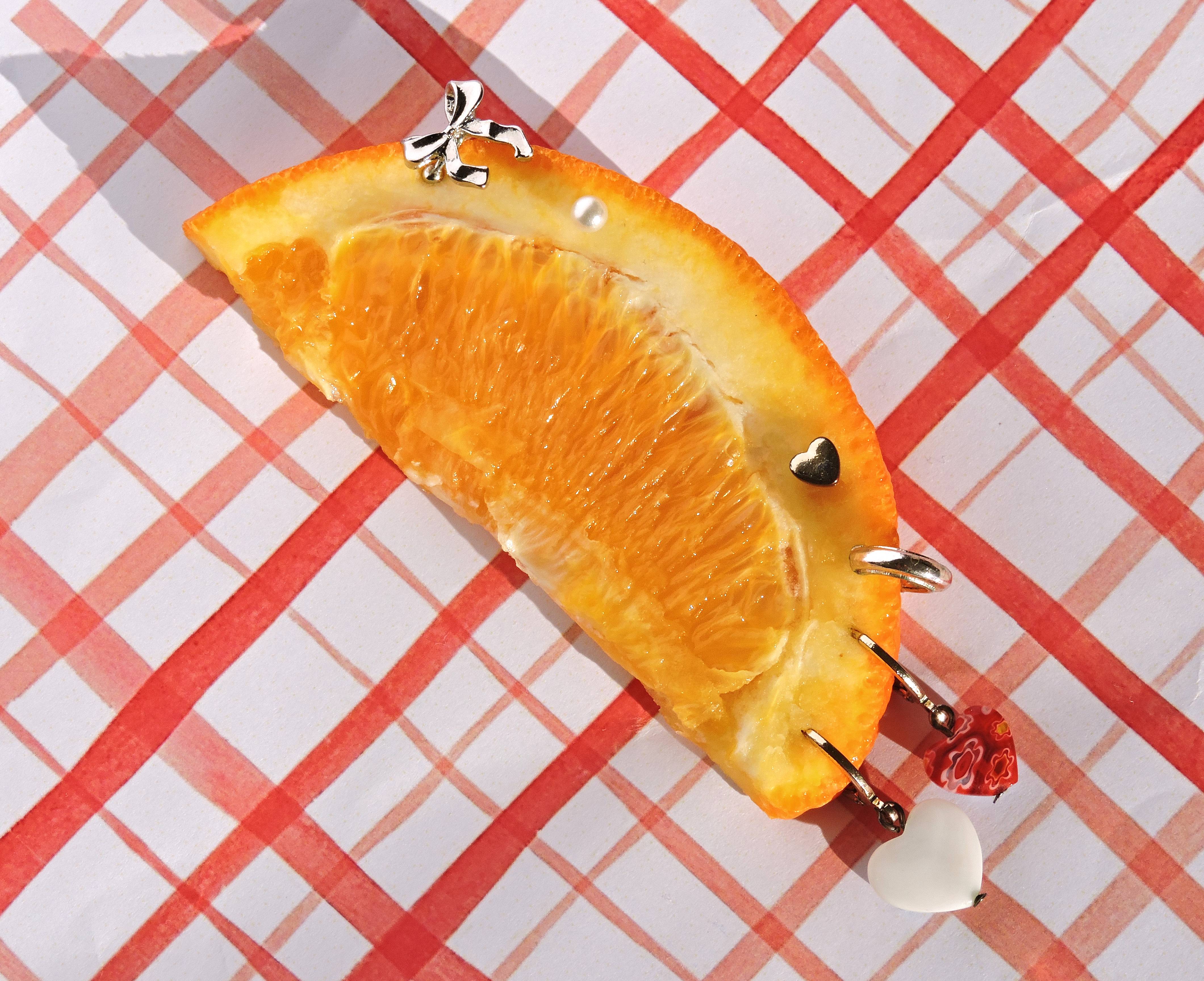 Gajo de naranja sobre mantel de cuadros rojo con piezas de joyería